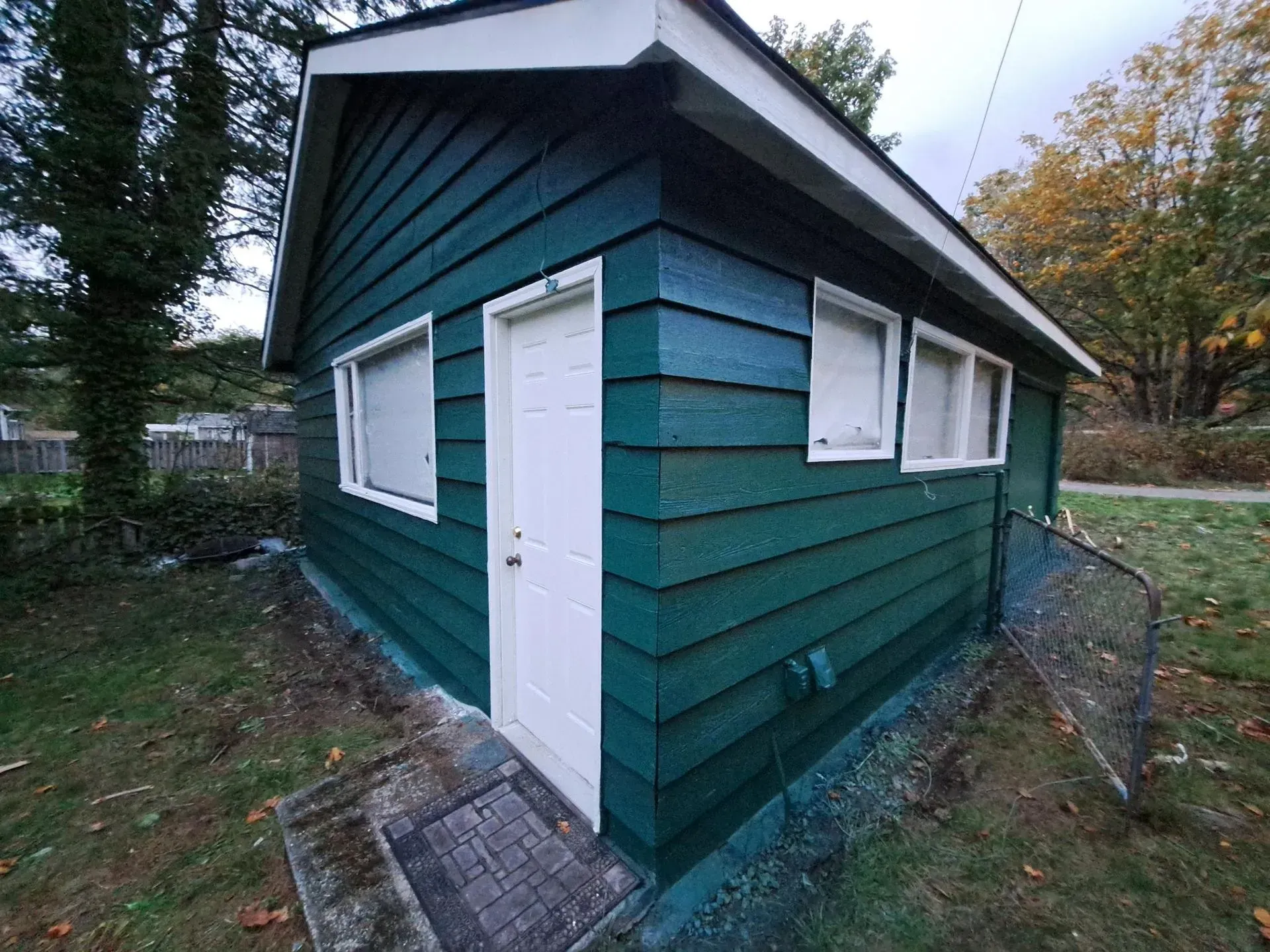 Green-painted shed with white door and windows on a grassy lawn.