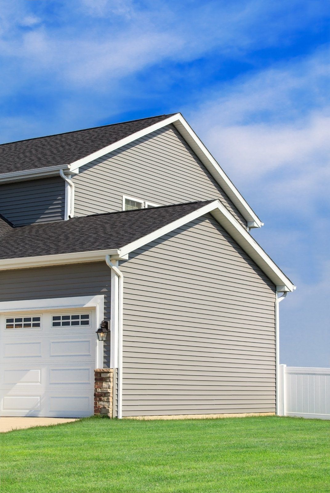 Gray house with white trim and garage door against a blue sky, set on green grass.