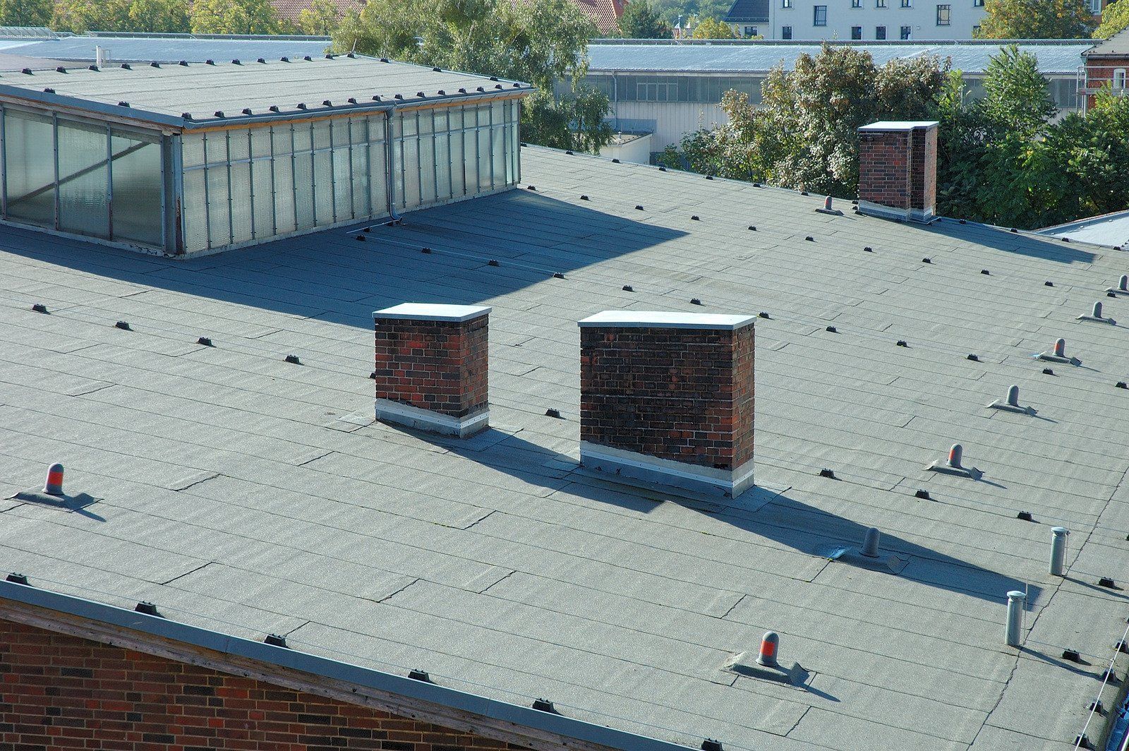 Brick chimneys on a flat roof with a glass skylight and trees in the background.