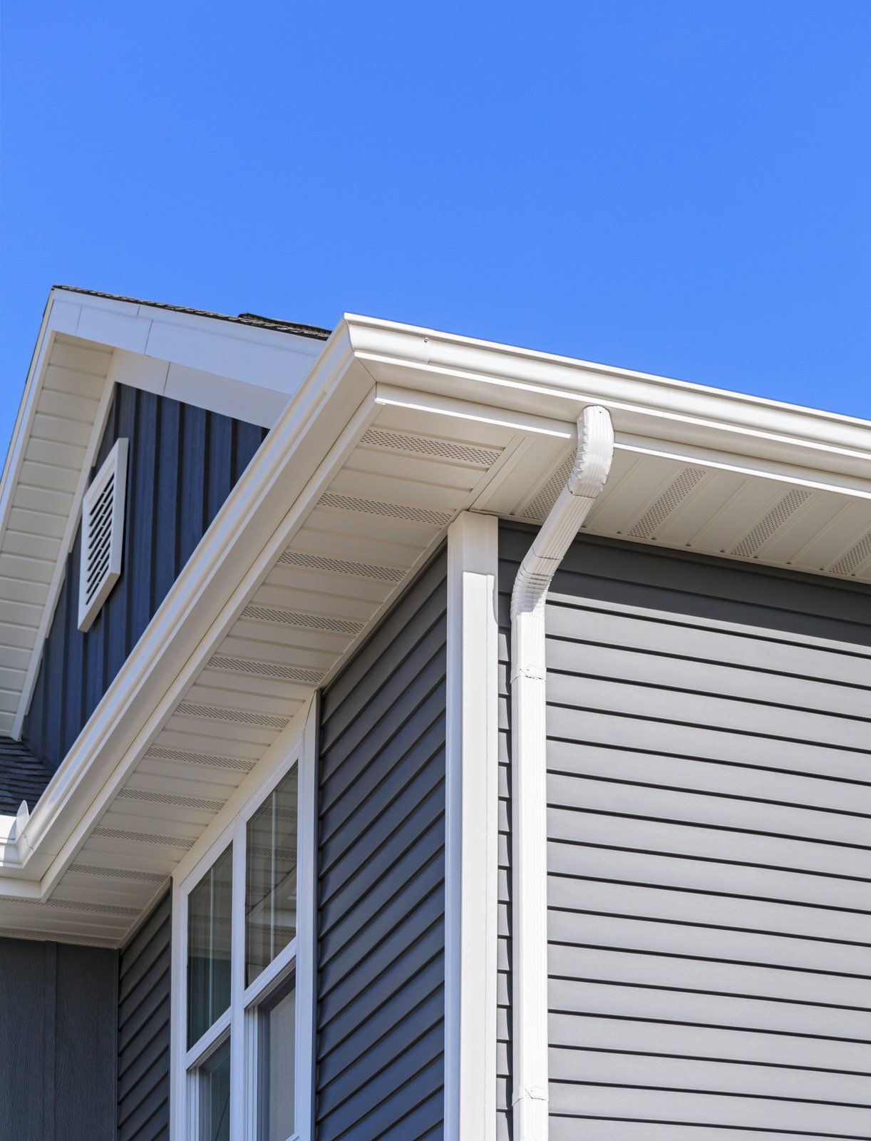 Exterior view of a house with blue-gray siding, white trim, and a clear blue sky.