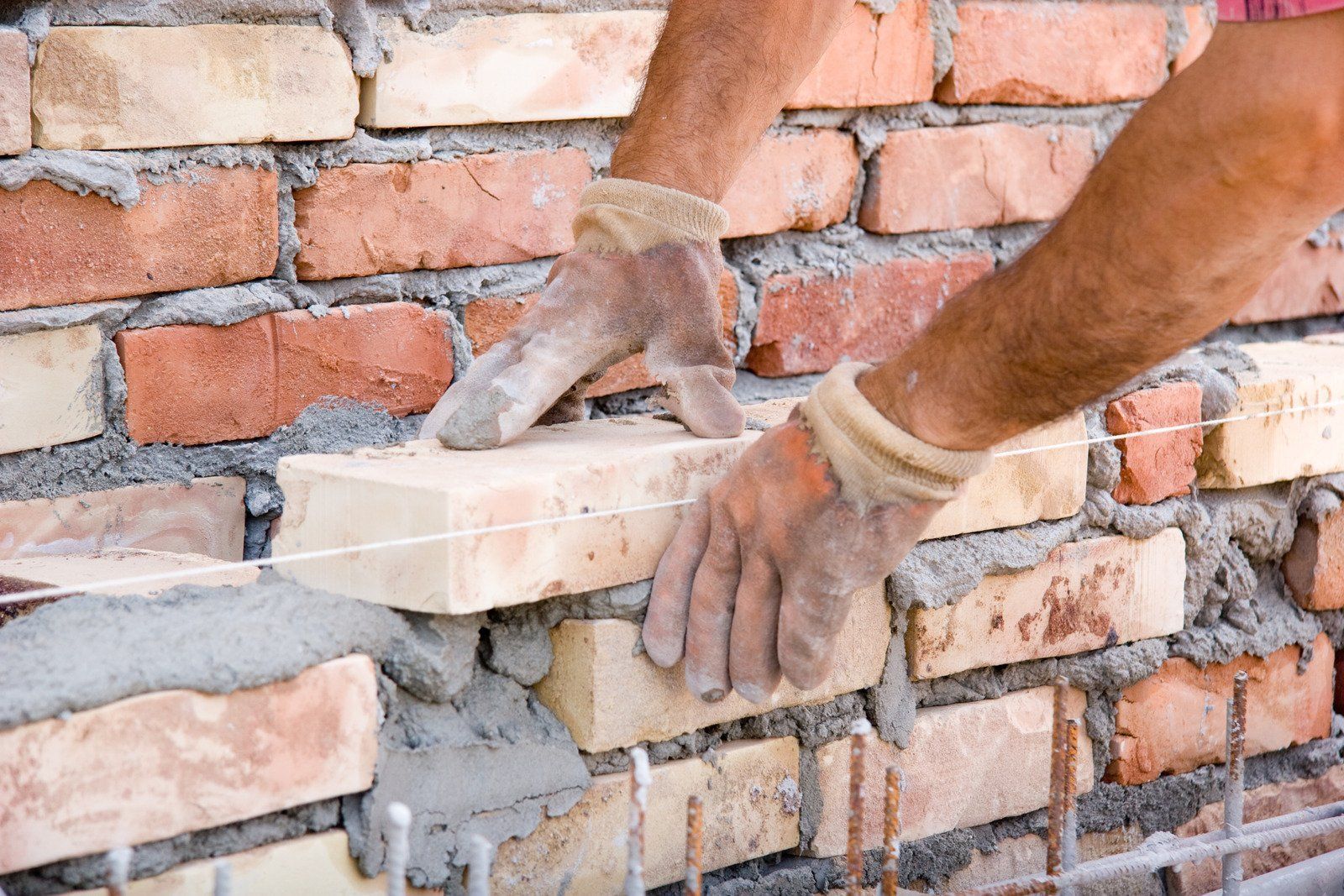 Hands laying a brick, part of a brick wall being constructed with mortar.
