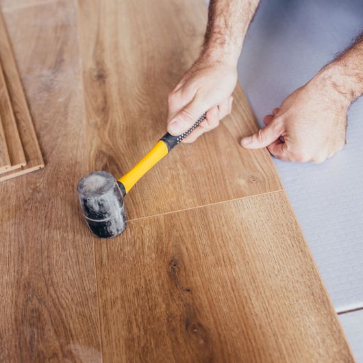 Palma Construction LLC | A person is holding a rubber mallet on a wooden floor.