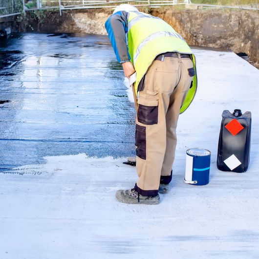 Palma Construction LLC | A man in a safety vest is painting a concrete surface