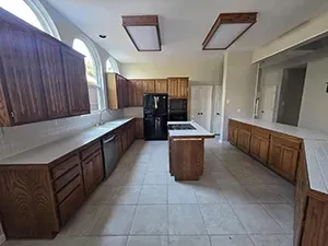 Empty kitchen with dark wood cabinets, white tile floor, black appliances, and a central island under skylights