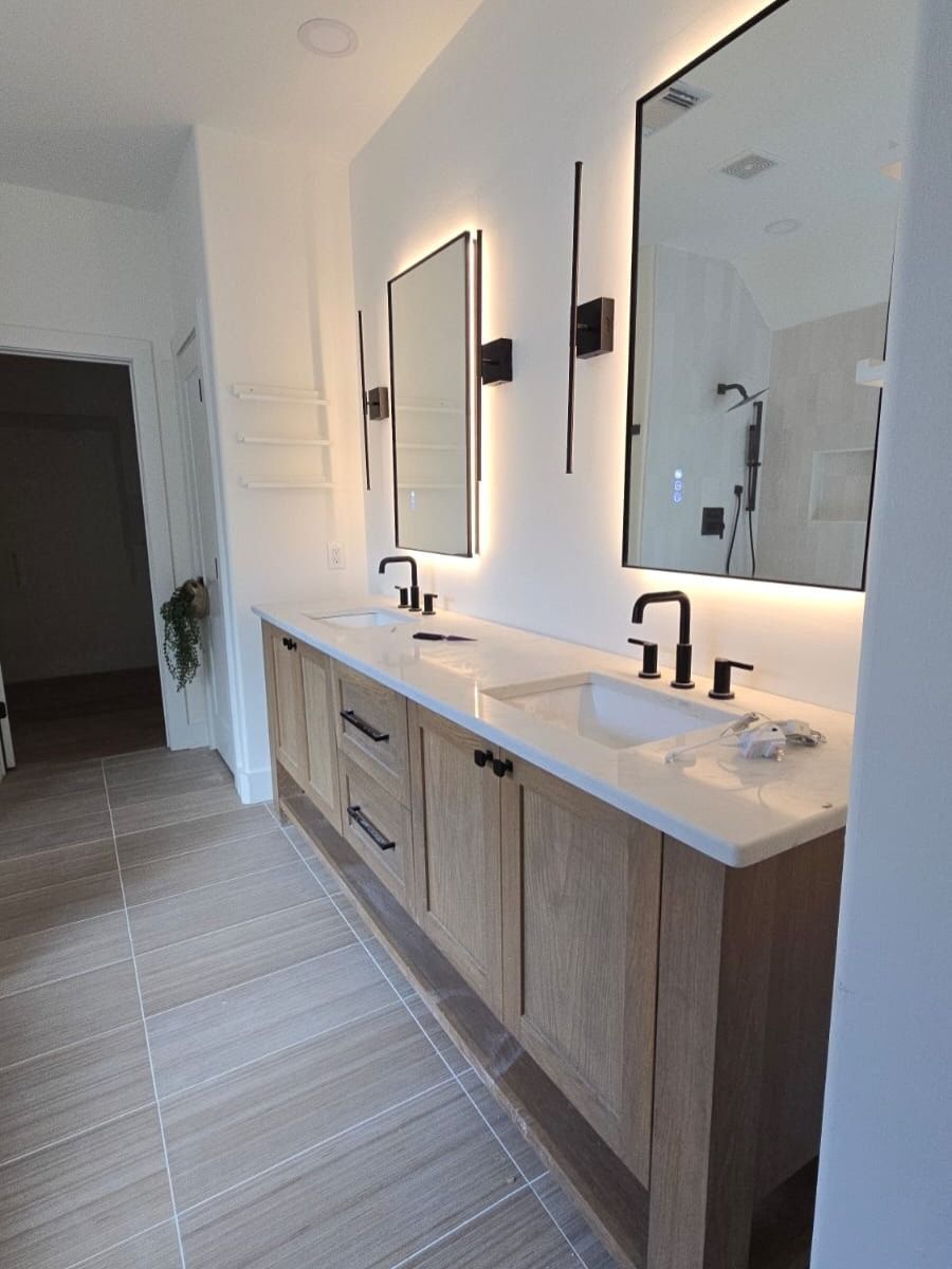 Modern bathroom with double vanity, large mirrors, wall sconces, and light wood cabinetry