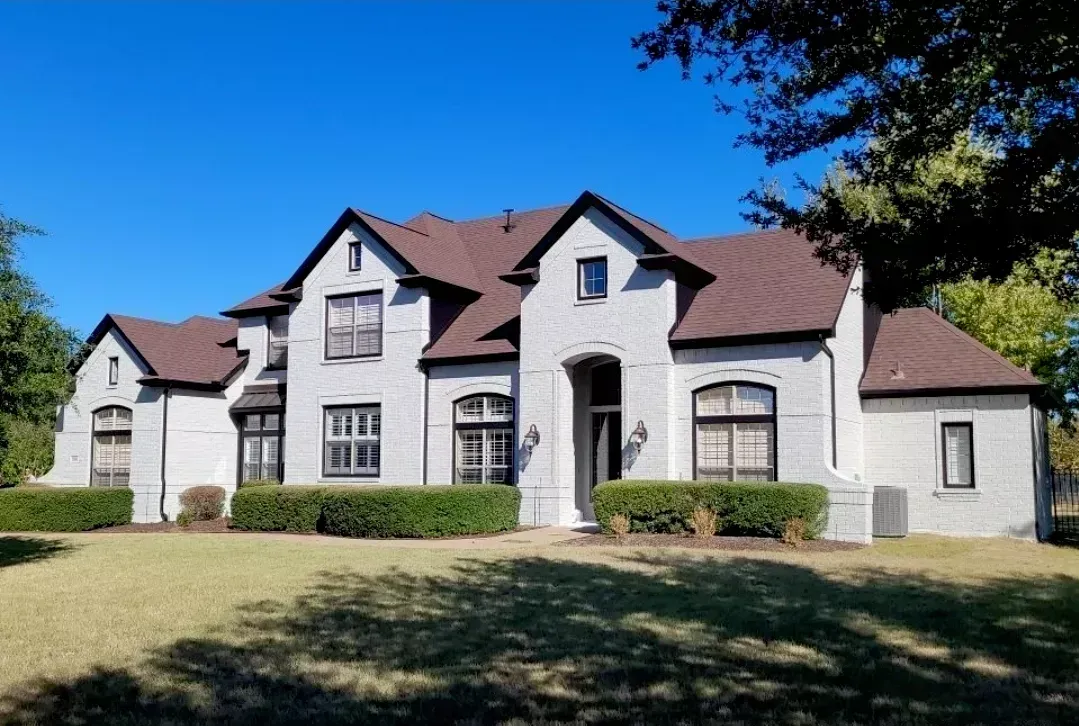 Large white stucco house with brown roof and arched entry, viewed from a grassy front yard under a blue sky