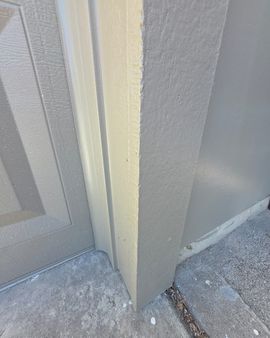 Close-up of a building corner with beige and gray siding beside a concrete walkway.
