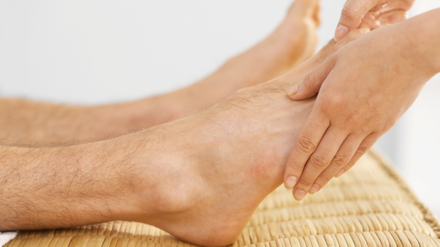 Person receiving ankle massage; hands are applying pressure, close-up shot of feet.
