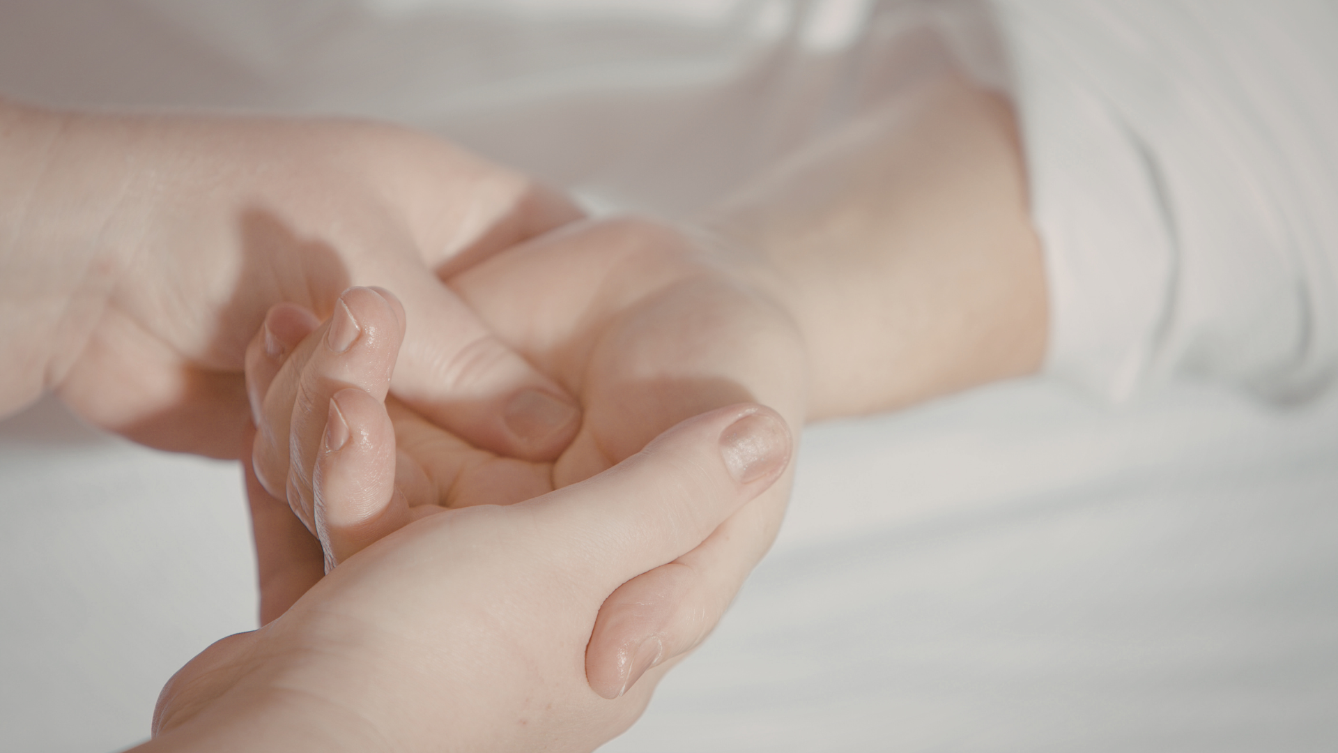Hands gently holding another hand, possibly giving a massage, on a white surface.