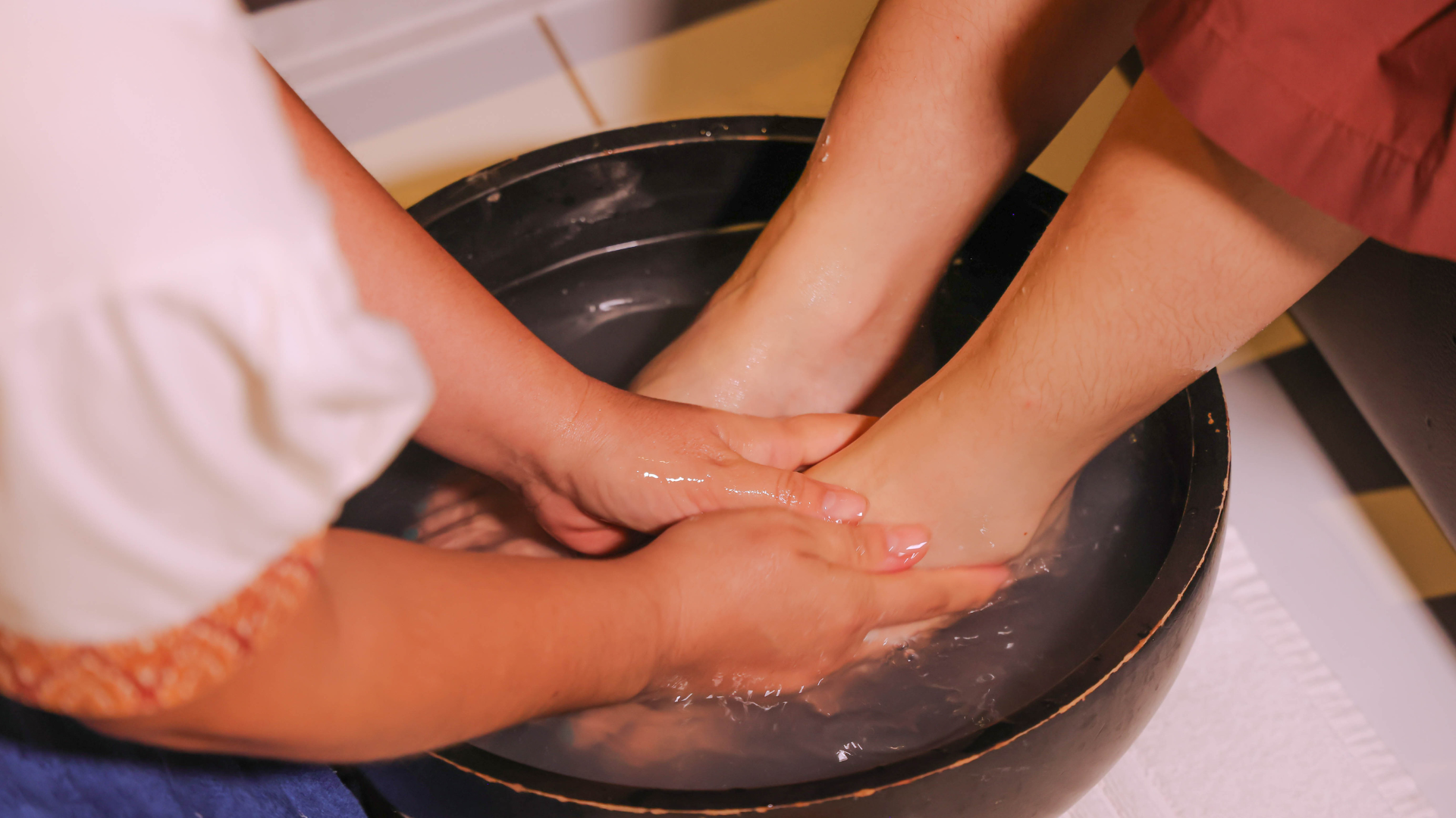 Hands massaging feet submerged in water inside a black bowl.