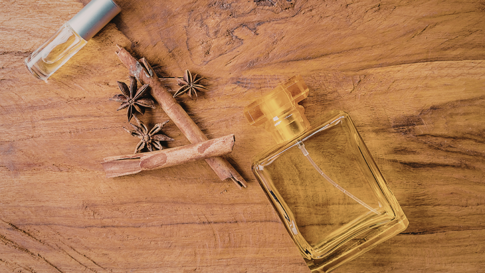 Perfume bottles, star anise, and cinnamon sticks on a wooden surface.