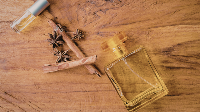 Perfume bottles, star anise, and cinnamon sticks on a wooden surface.