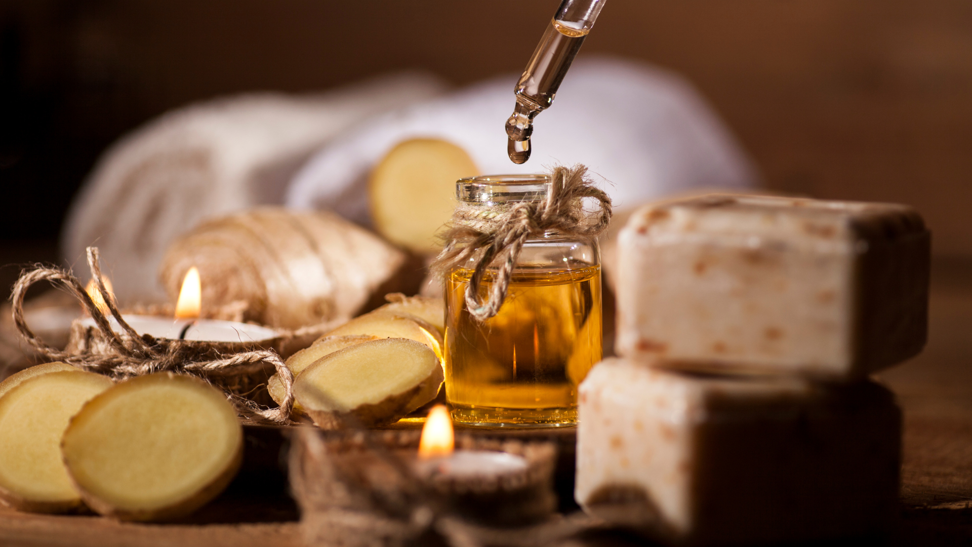 Ginger oil bottle with a dropper, candles, soap, and ginger slices; spa setting.