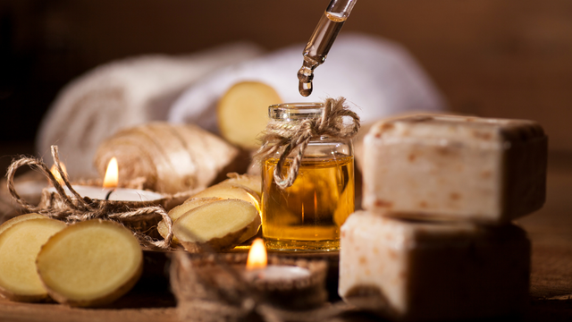 Ginger oil bottle with a dropper, candles, soap, and ginger slices; spa setting.