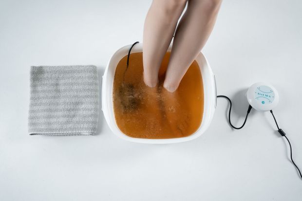 Foot massage with wooden tool. Hands applying pressure to oiled foot. Soft lighting.