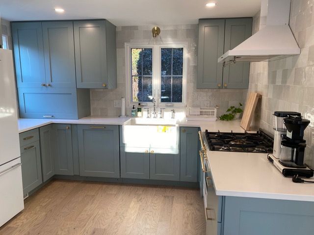 A kitchen with blue cabinets , white counter tops , a stove and a sink.