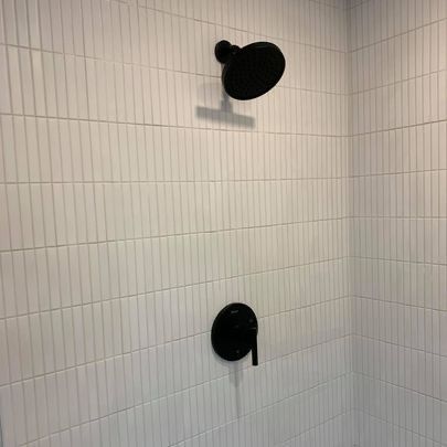 A shower with white tiles and black shower heads.