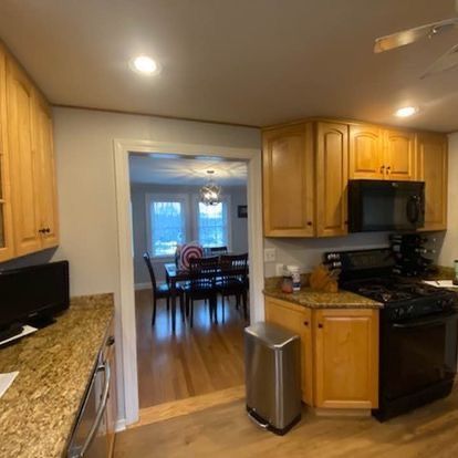 A kitchen with wooden cabinets , granite counter tops , a stove , microwave , and a trash can.