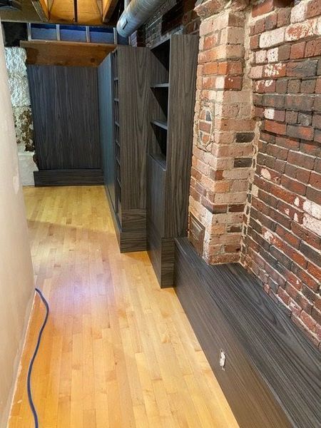 A hallway with hardwood floors and a brick wall.