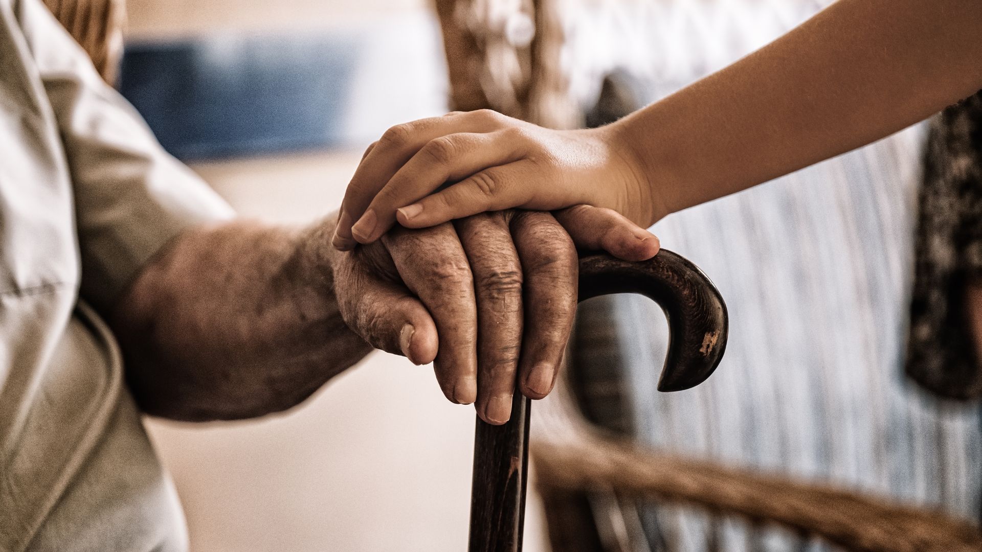 A young girl is holding the hand of an older man holding a cane.