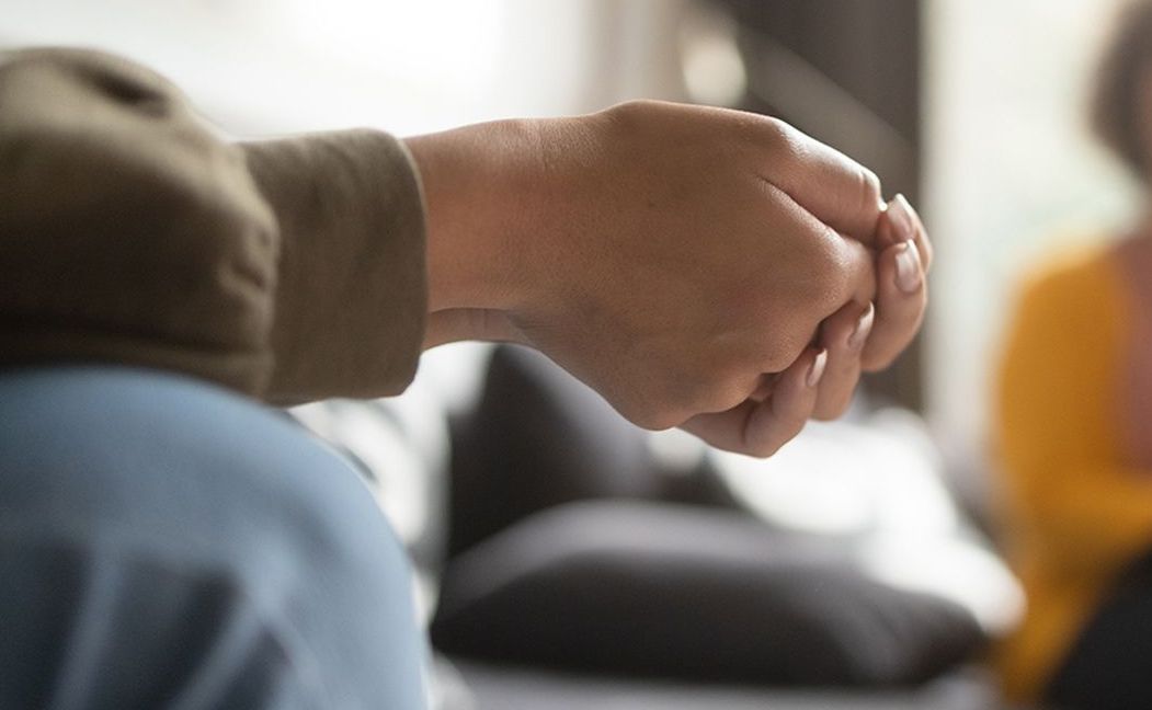 A man in a green hoodie is standing on the beach with his eyes closed.