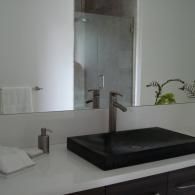 A modern bathroom vanity with a black rectangular sink, brushed nickel faucet, and white countertop in front of a mirror.
