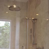 A walk-in shower with a rainfall showerhead, handheld sprayer, and neutral tiled walls next to a window.