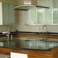 Modern kitchen featuring a wooden island with a black countertop, stainless steel faucets, and glass-front cabinets.