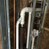 White PVC plumbing pipes, including a Y-joint and a Fernco coupling, installed within unfinished metal wall studs.