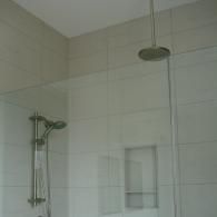 A modern shower stall featuring a rainfall showerhead, a handheld shower fixture, and an inset wall niche for storage.