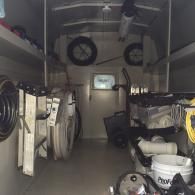 The cluttered interior of a work van filled with tools, ladder, spare tires, pipes, and buckets.