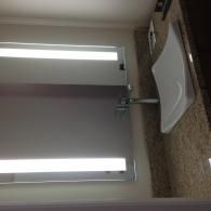 A modern bathroom vanity with a white vessel sink on a granite countertop, featuring a mirror with integrated lighting.