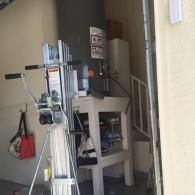 A silver hand-crank material lift stands in a garage next to a water heater and a white utility shelf.