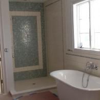 A bathroom featuring a freestanding white tub next to a walk-in shower with light blue mosaic tiles and white trim.