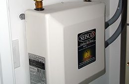 A beige Seisco tankless electric water heater mounted on a wall with pipe connections visible.
