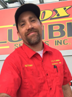 A person with a beard and baseball cap wearing a red work shirt with 