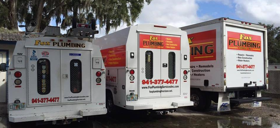 Three white Ems Plumbing trucks parked side-by-side outdoors, showing company branding and phone number.