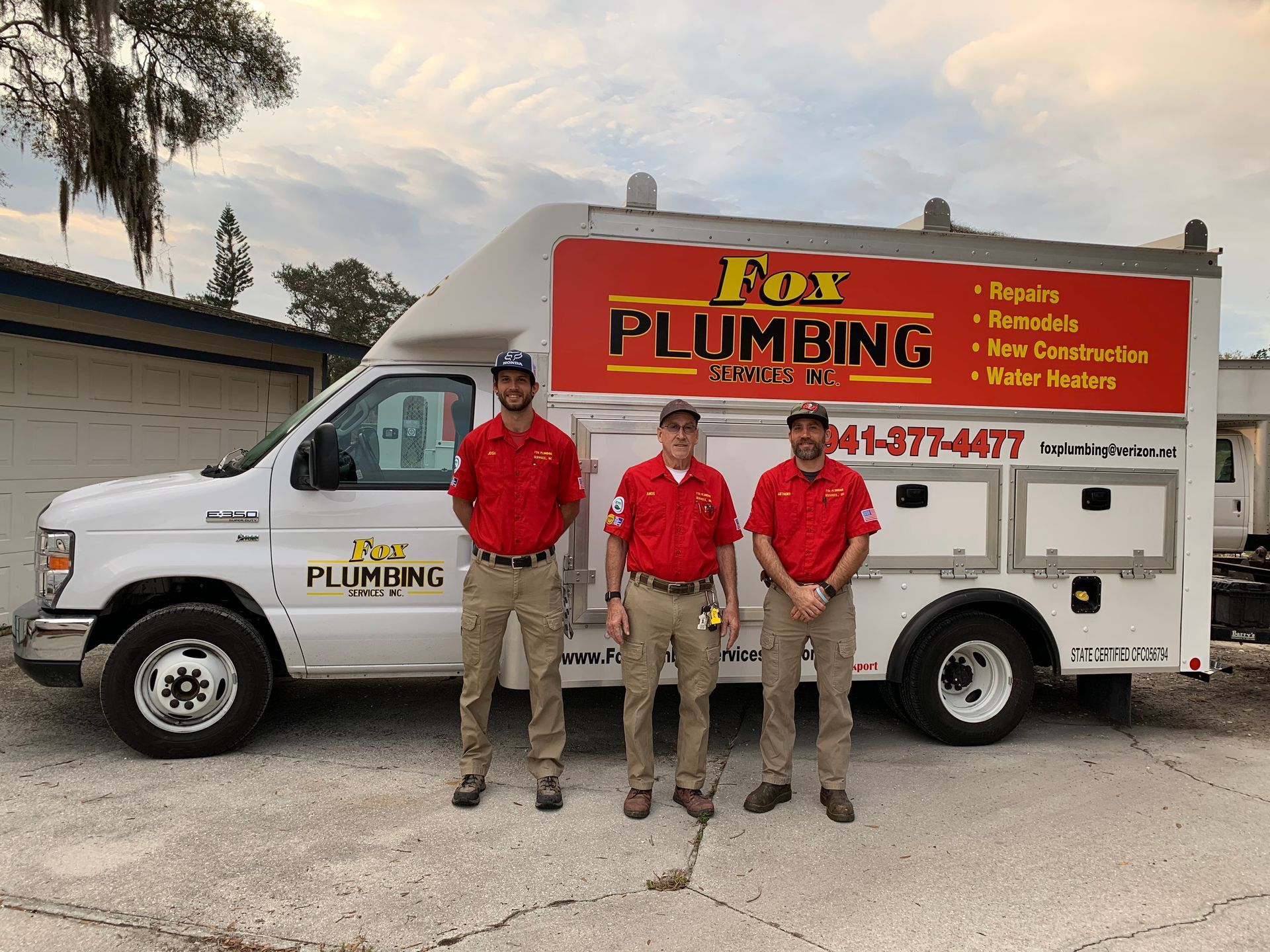Three people in red uniforms stand in front of a white Fox Plumbing service truck, parked on an asphalt lot.