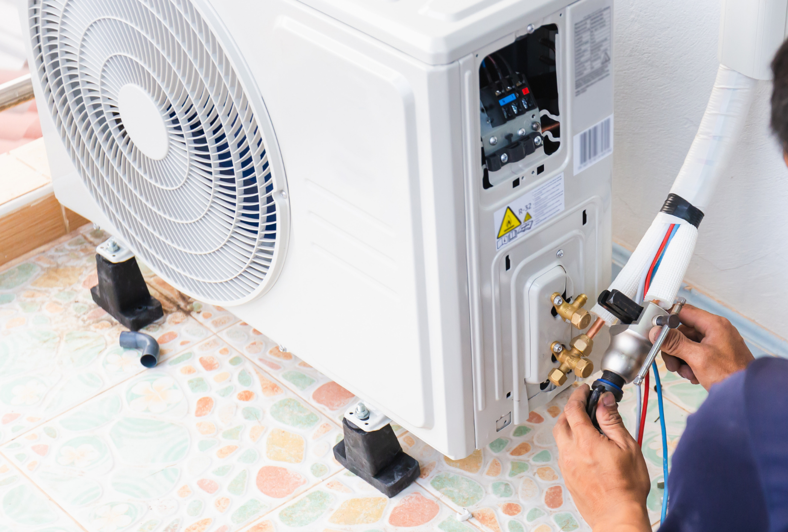 Technician repairing an outdoor air conditioner unit with tools and cables.