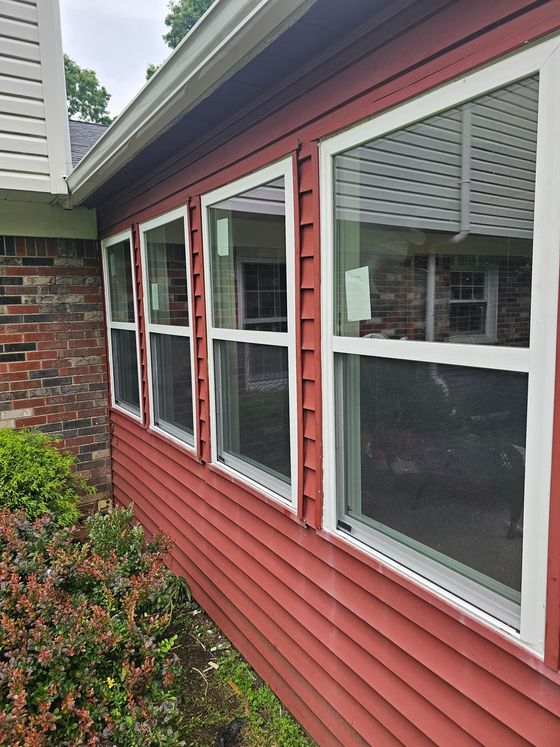 Red house exterior with white-trim windows and a brick corner beside shrubs.