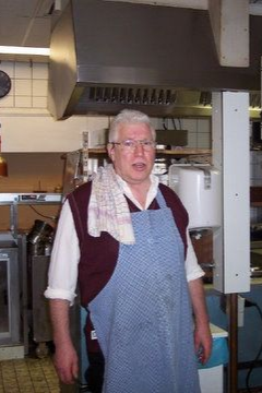 Een man met een schort staat met een handdoek in een professionele keuken.