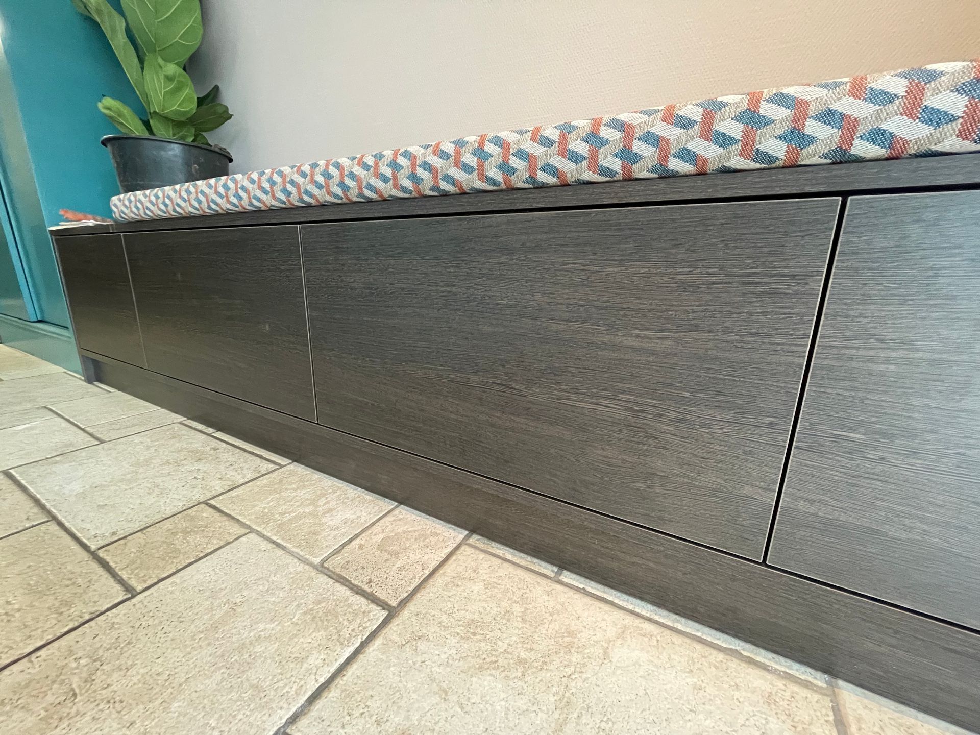 Donkerhouten opbergbank met kussen met patroon op een tegelvloer.