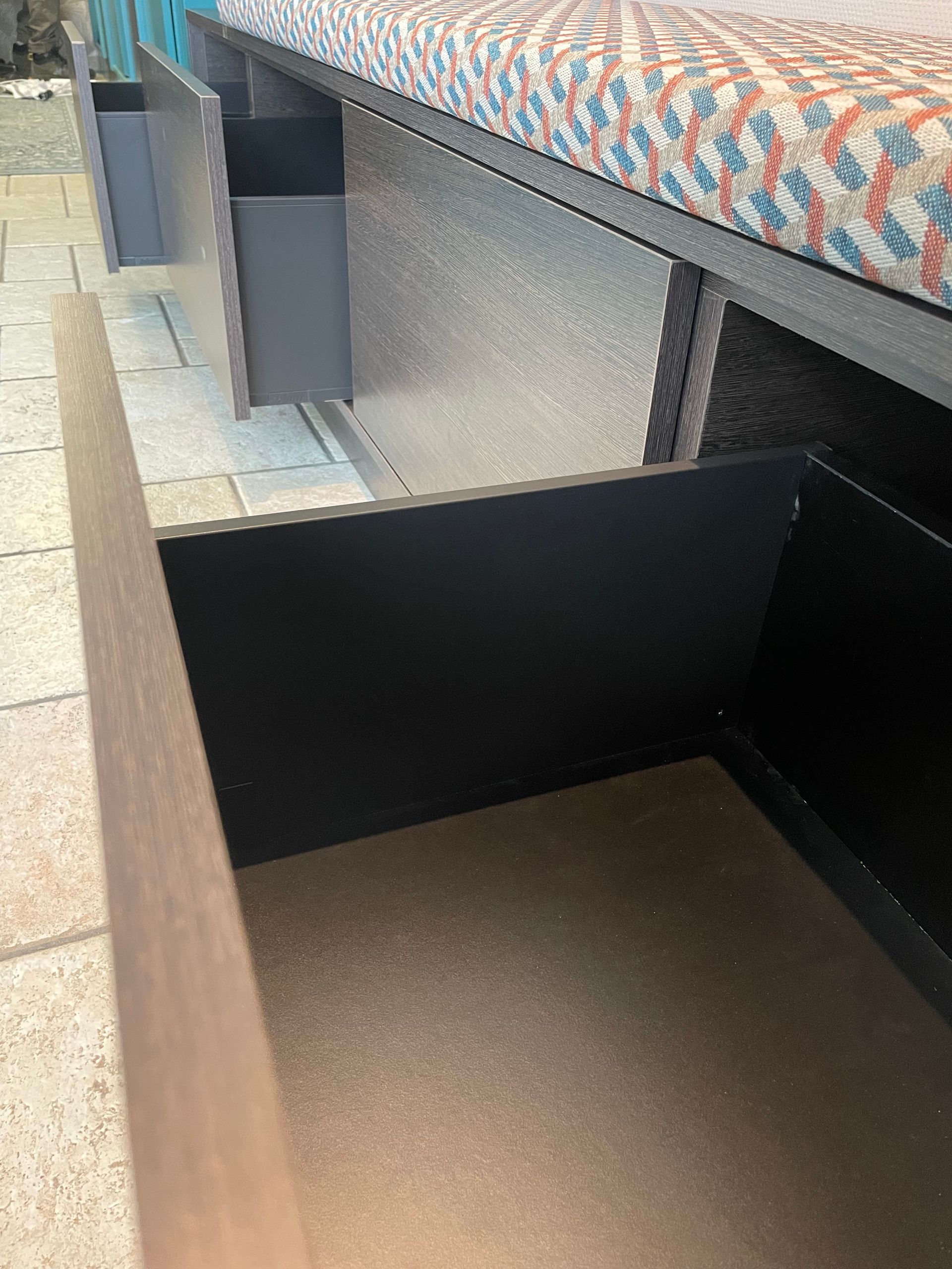 Open lade in een ingebouwde bank met opbergvakken; de binnenkant is uitgevoerd in zwart en beige.