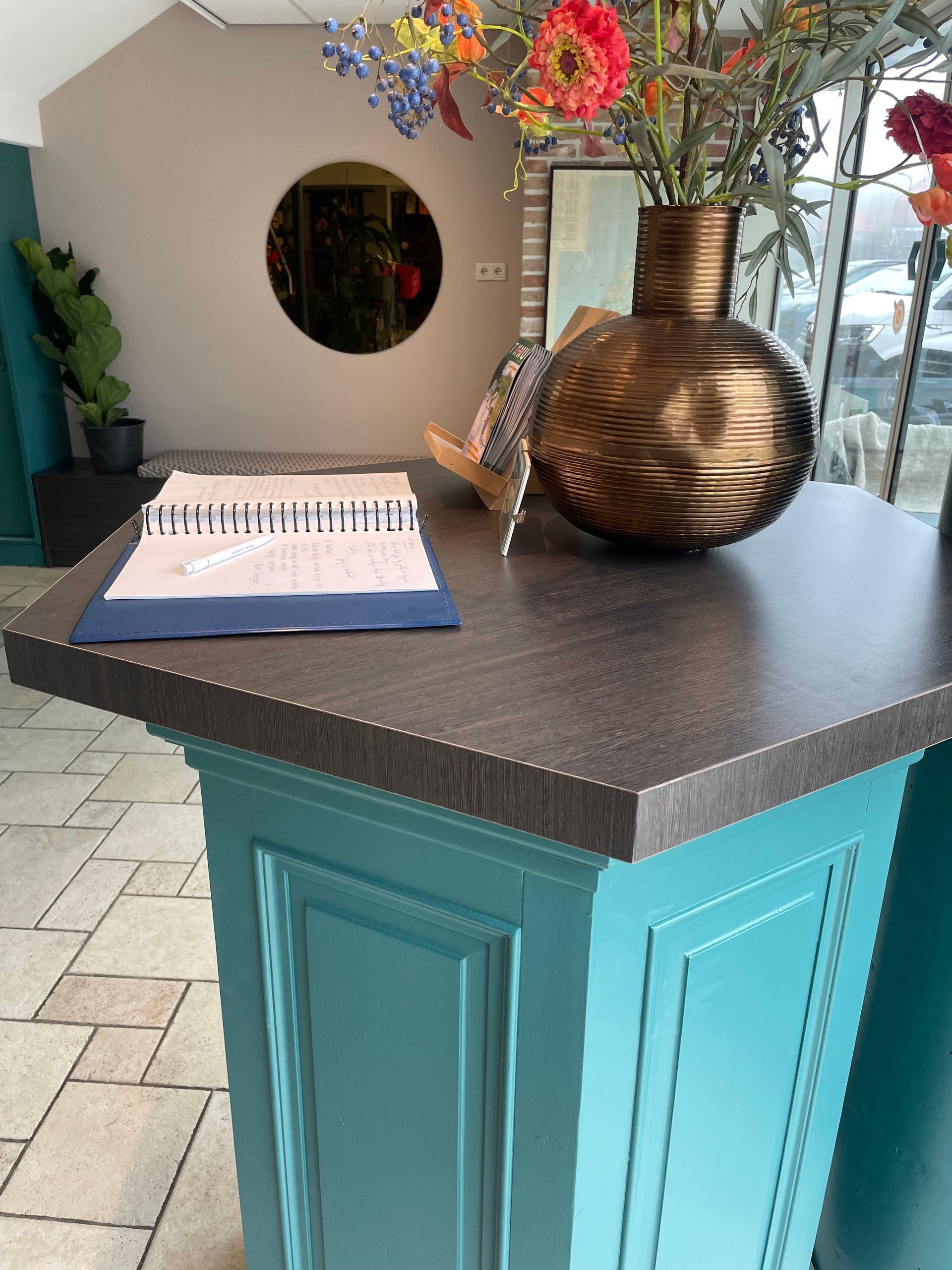 Een turquoisekleurige toonbank met een donker aanrechtblad, een vaas met bloemen en een notitieboekje in een kantoor.