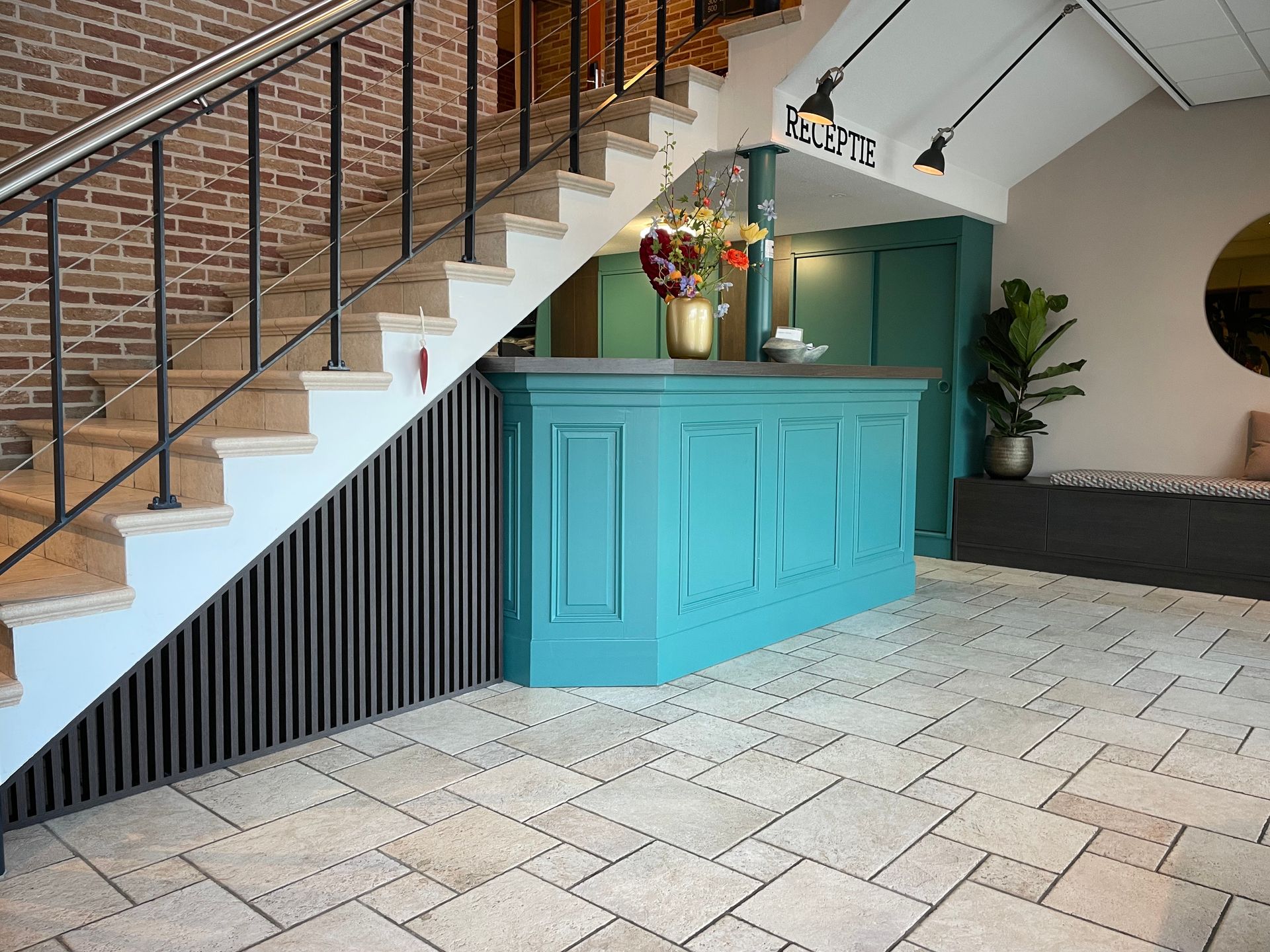 Hotellobby met receptie en trap. Turquoise balie, bakstenen muur, tegelvloer, trap.