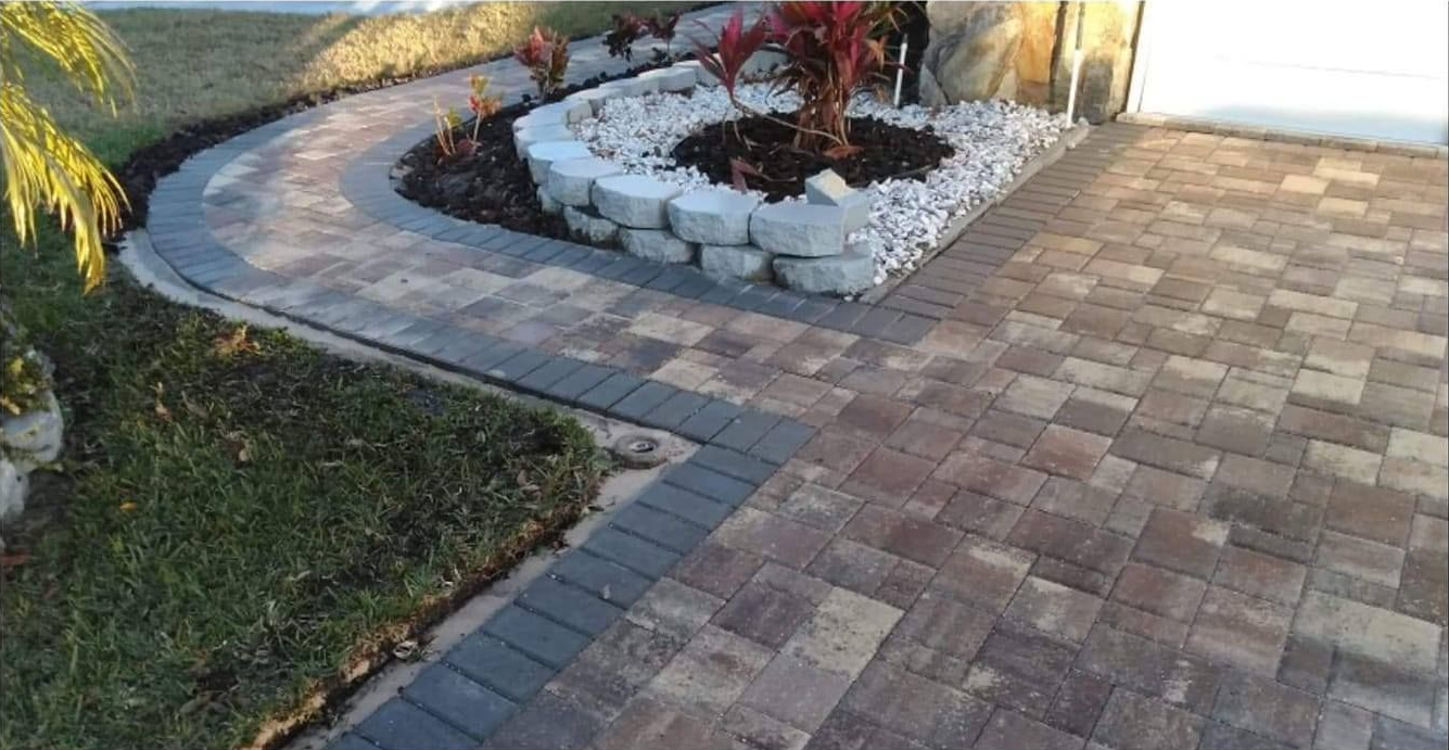 Paver walkway curves past a rock garden and connects to a driveway.