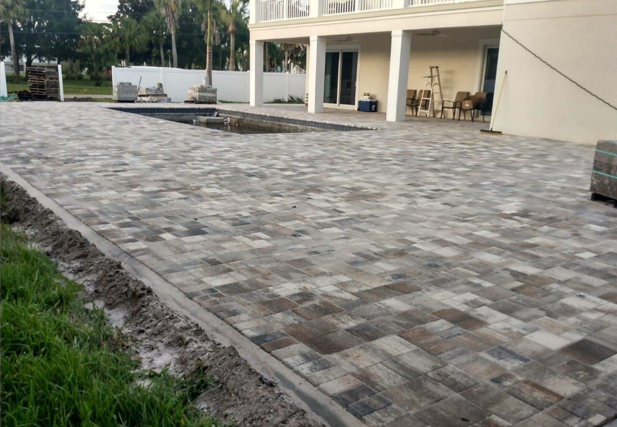 Brick pavers on a patio with a swimming pool and a white house.