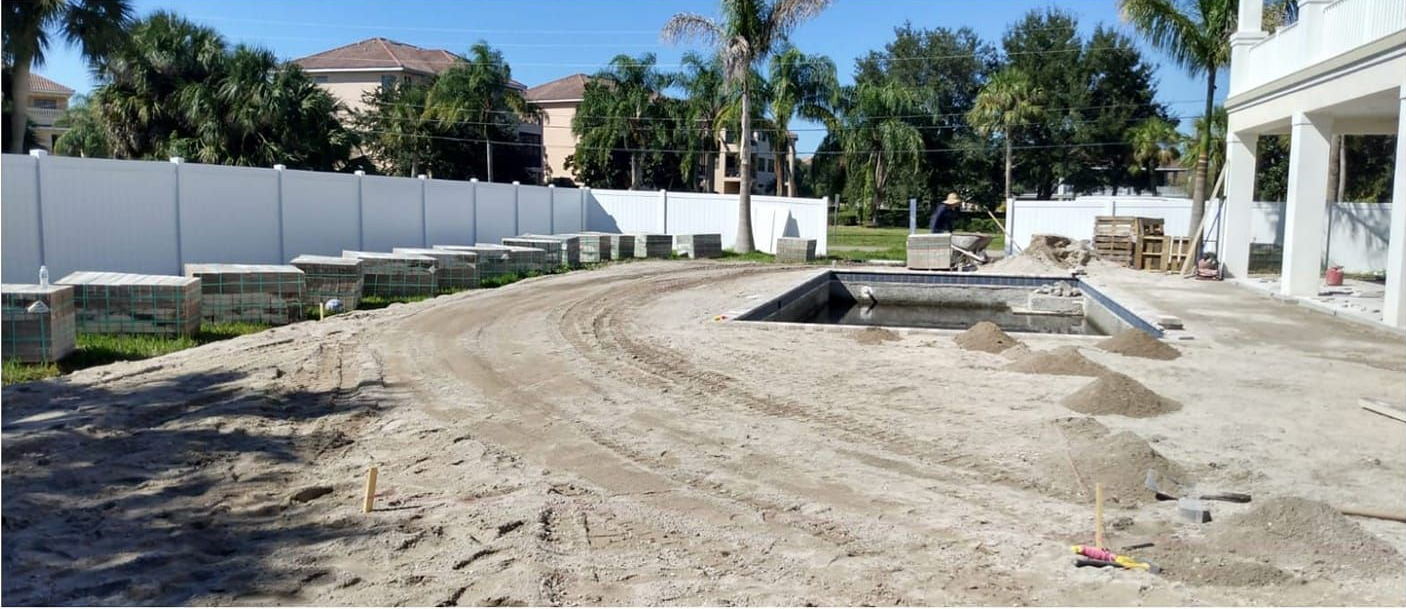 Construction site with a partially built swimming pool and white fence.