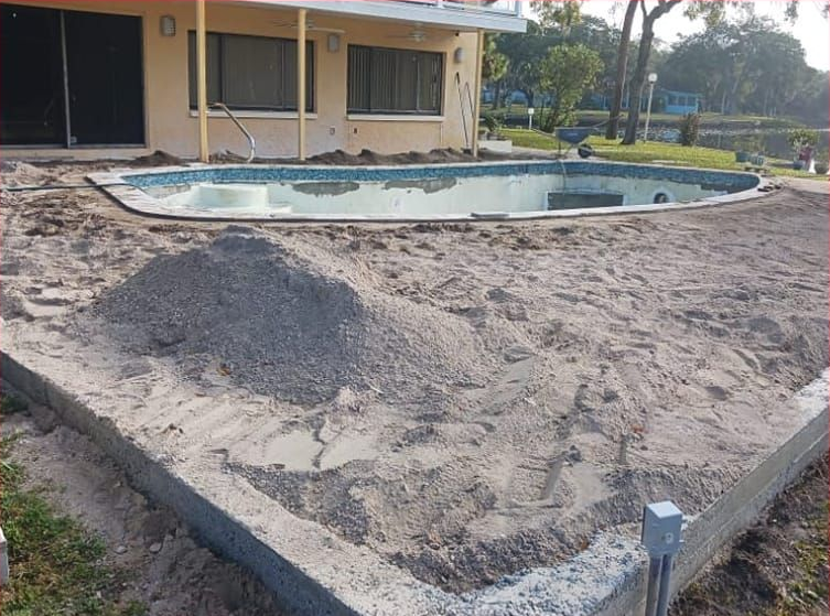 Pool renovation in progress: pool basin, sand, gravel pile, and house in the background.