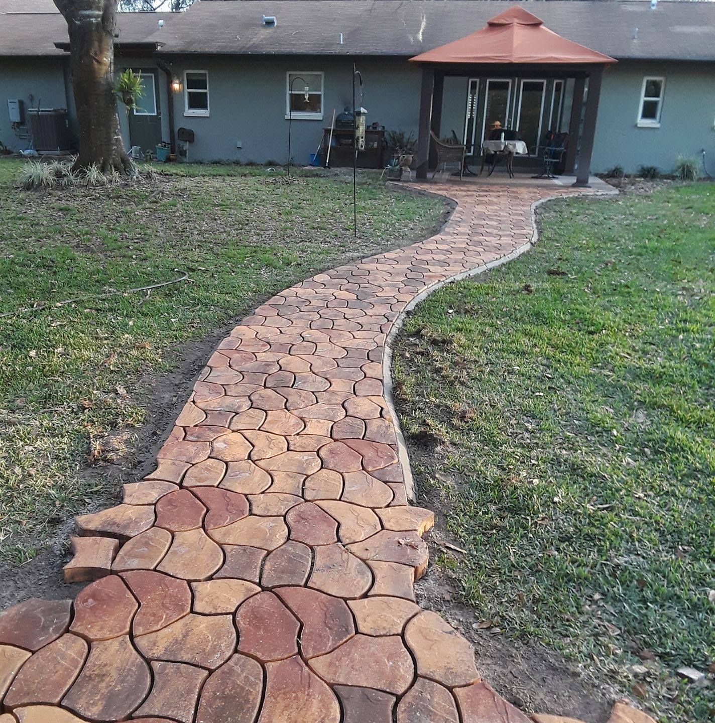 A winding brick path leads to a gazebo in a backyard with a house in the background.
